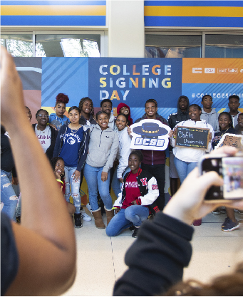 Large group of students posing with signs with college logos