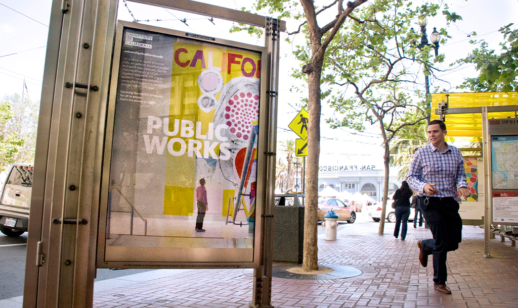 Bus shelter with poster of a person standing in front of a indoor mural and the words Public Works